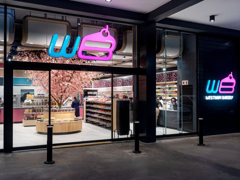 Westham Bakery Overport storefront at night with glowing neon signage and cherry blossom tree inside the store.